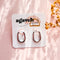 A pair of Agaveh Girl Silver Layla Hoops, featuring a chunky, rounded oval design, displayed on a branded card with the text 'agaveh girl,' against a textured background. The earrings are minimalist and modern, available in Ottawa, Ontario, Canada.