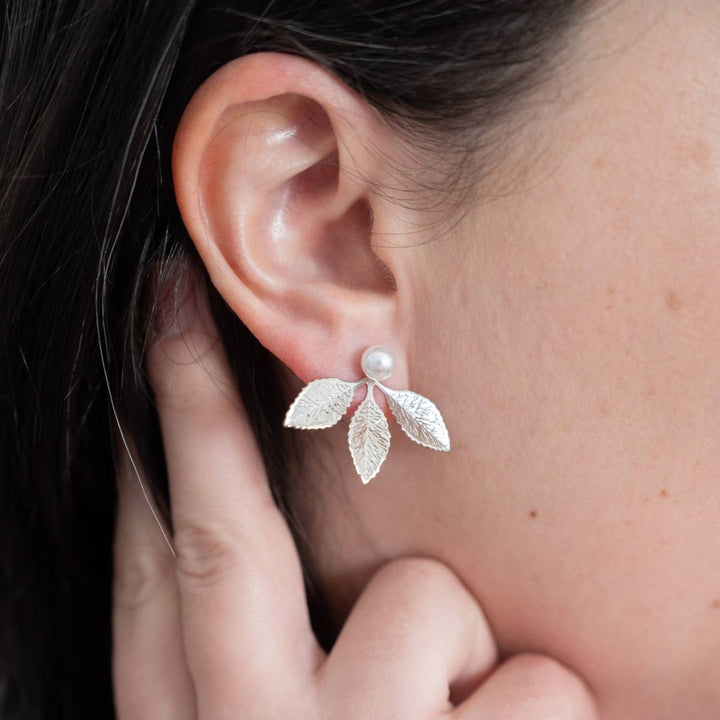 A pair of silver leaf earrings with detachable ear jackets. The earrings feature three overlapping leaf-shaped designs with a small pearl in the center of each leaf. 