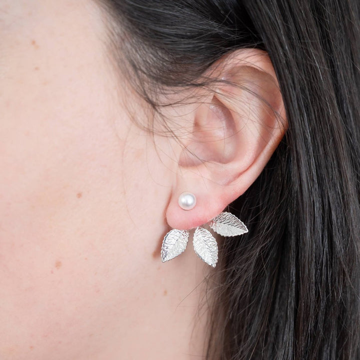 A pair of silver leaf earrings with detachable ear jackets. The earrings feature three overlapping leaf-shaped designs with a small pearl in the center of each leaf. 