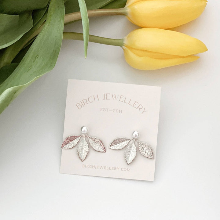 A pair of silver leaf earrings with detachable ear jackets. The earrings feature three overlapping leaf-shaped designs with a small pearl in the center of each leaf. 