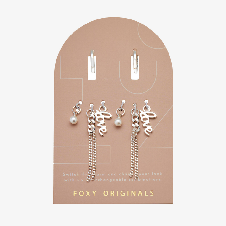 A set of silver earrings with interchangeable charms. The set includes two pairs of silver hoop earrings and three charms: a pearl, the word 