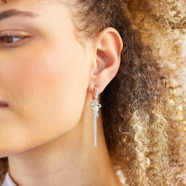 A set of silver earrings with interchangeable charms. The set includes two pairs of silver hoop earrings and three charms: a pearl, the word 