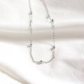 A silver chain necklace with multiple small, round beads evenly spaced along the chain. The necklace is resting on a white surface.