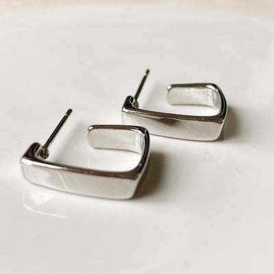 A pair of silver squared hoop earrings, featuring a chunky, geometric square design, displayed on a white, textured surface. The earrings are modern and minimalist, available in Ottawa, Ontario, Canada.