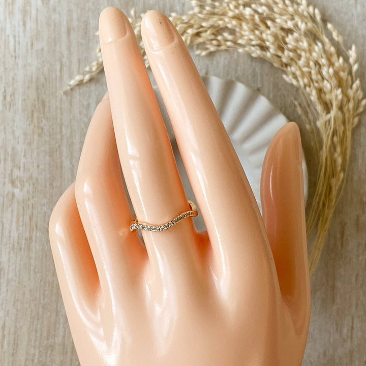 A silver Tidal Wave ring, featuring a wavy, curved design with pave diamonds, displayed on a light wooden surface with a blurred white ceramic element in the background. The ring is a curved wedding band or stacking ring, available in Ottawa, Ontario, Canada.