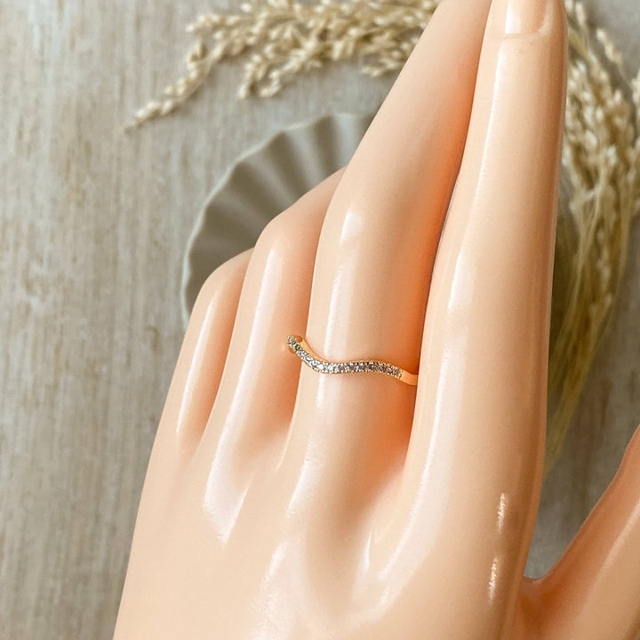 A silver Tidal Wave ring, featuring a wavy, curved design with pave diamonds, displayed on a light wooden surface with a blurred white ceramic element in the background. The ring is a curved wedding band or stacking ring, available in Ottawa, Ontario, Canada.