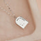 A silver necklace with a pendant shaped like an archway. The pendant has the words 