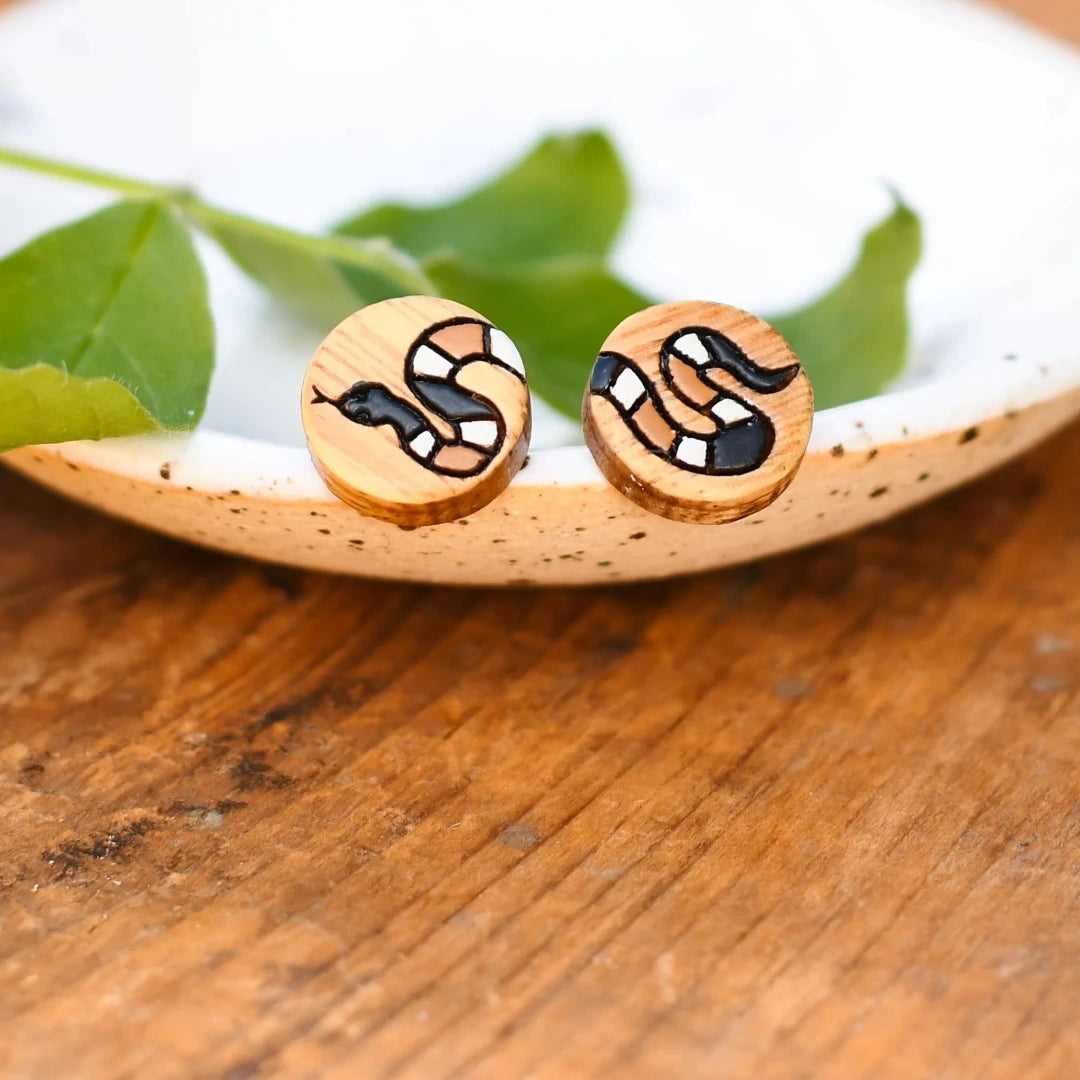 A pair of wooden earrings featuring a snake design in brown, black, and white.