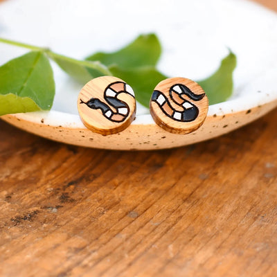 A pair of wooden earrings featuring a snake design in brown, black, and white.