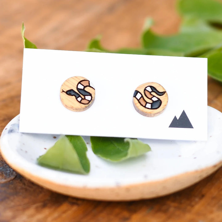 A pair of wooden earrings featuring a snake design in brown, black, and white.
