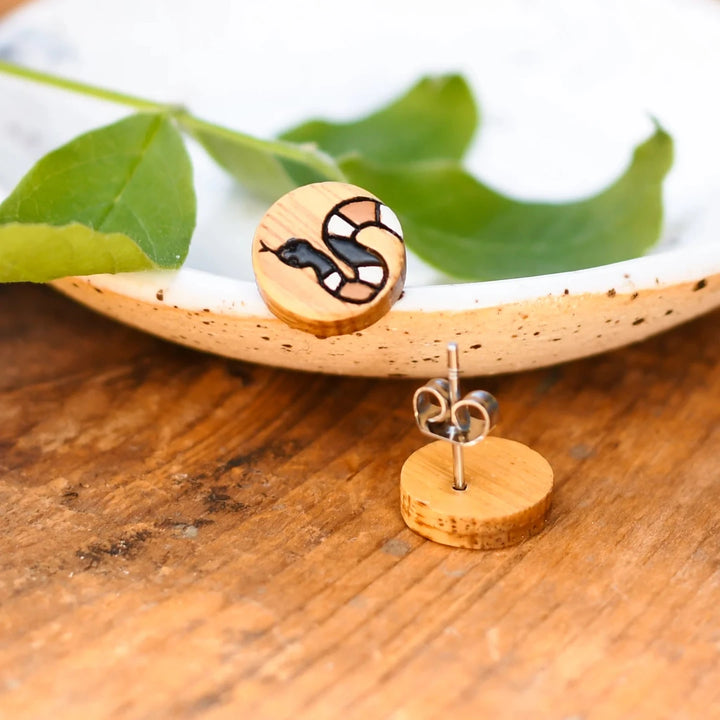 A pair of wooden earrings featuring a snake design in brown, black, and white.