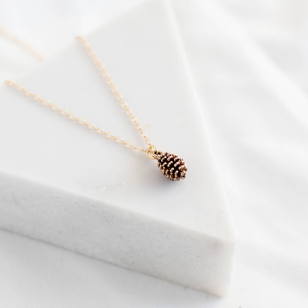 Gold necklace with a pine cone pendant on a white fabric background