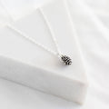 Silver pinecone necklace on a white fabric background