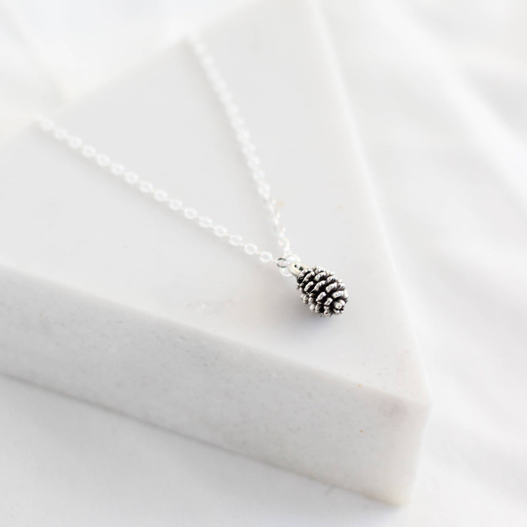 Silver pinecone necklace on a white fabric background