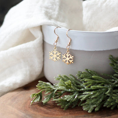 Gold snowflake earrings on a white cup with greenery