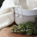 Silver snowflake earrings on a white cup with greenery