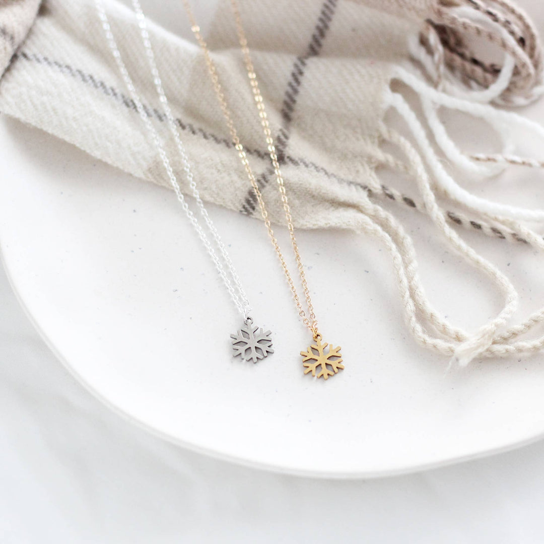 Two snowflake-shaped necklaces on a white plate with a neutral background