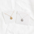 Two snowflake necklaces, one gold and one silver, on their respective cards with 'ARCH JEWELLERY' branding.