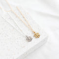 Two snowflake-shaped pendants on gold necklaces against a white textured background