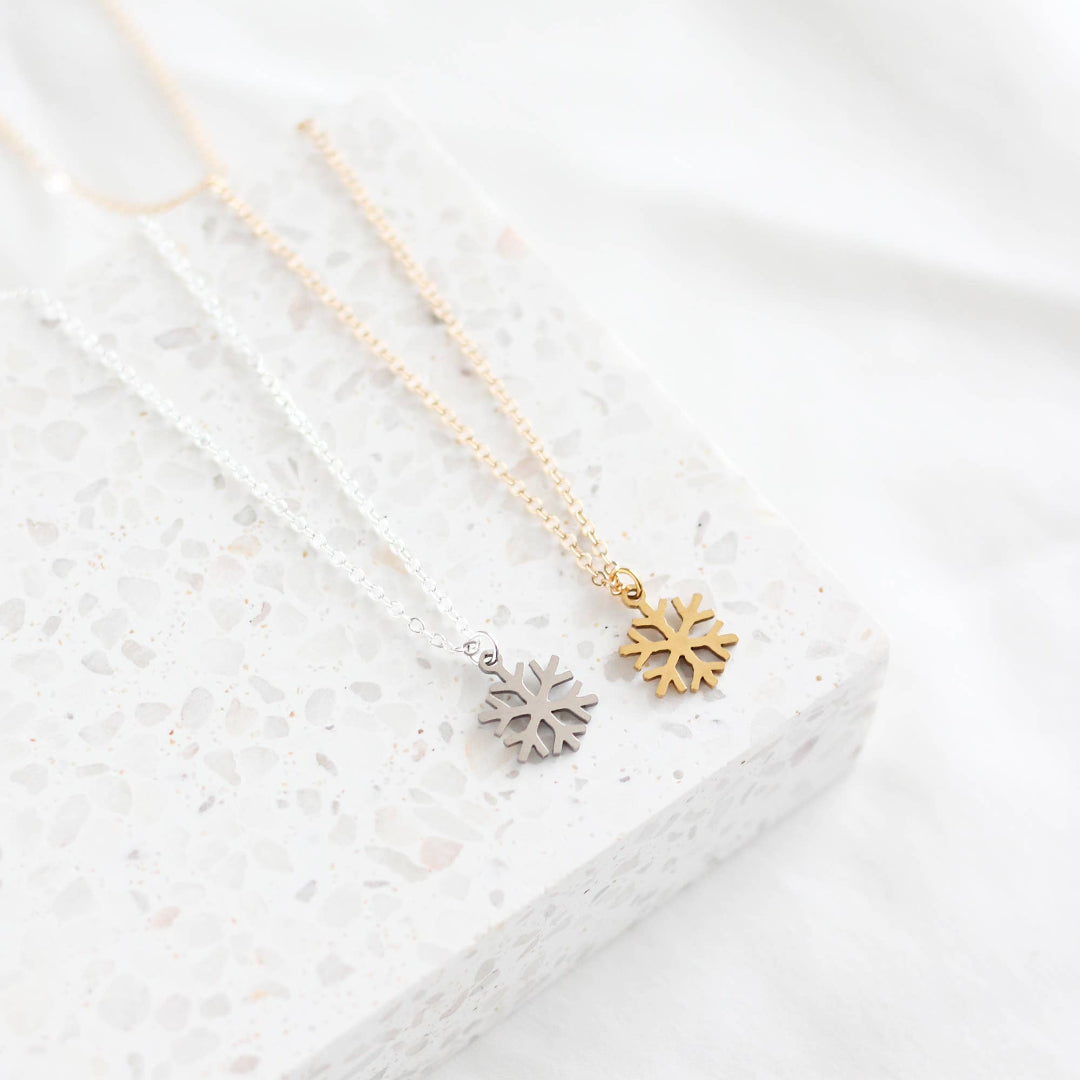 Two snowflake-shaped pendants on gold necklaces against a white textured background