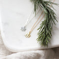 Two necklaces with snowflake pendants on a marble surface with greenery.
