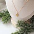Gold necklace with a snowflake pendant on a neutral background with greenery