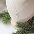 Silver snowflake necklace on a white stand with greenery