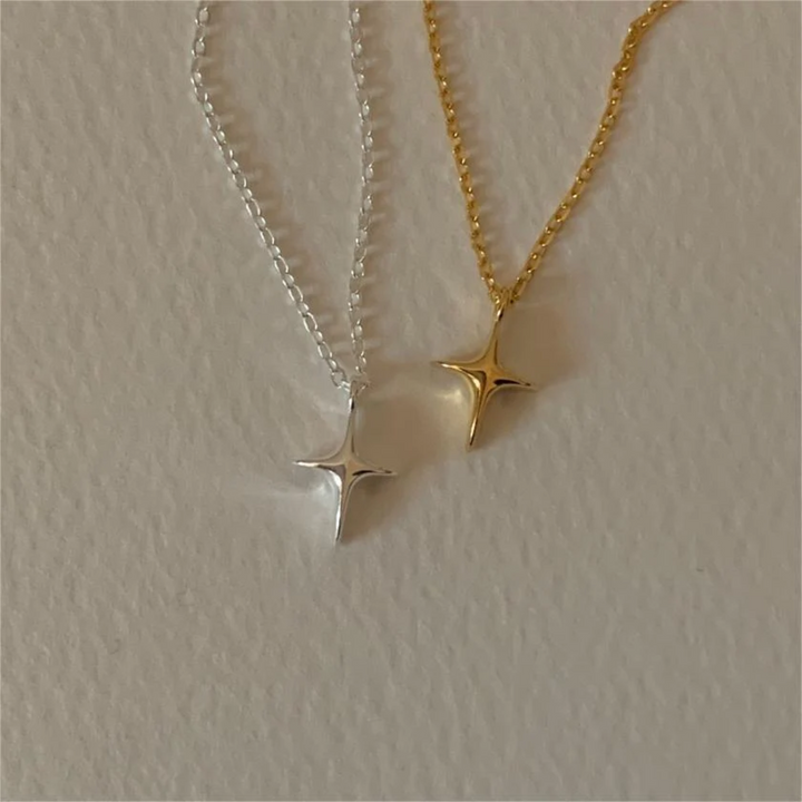 A set of silver and gold necklaces, each featuring a delicate chain and a minimalist four-pointed star or starfish-like pendant, resembling a sparkle emoji, displayed on a light surface. These celestial necklaces are available in Ottawa, Ontario, Canada.