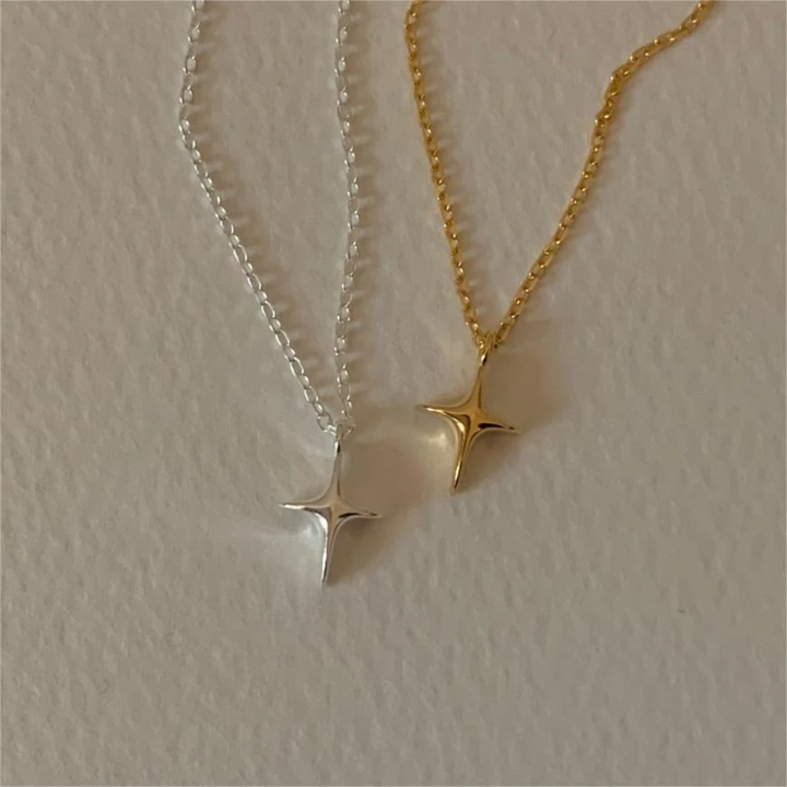 A set of silver and gold necklaces, each featuring a delicate chain and a minimalist four-pointed star or starfish-like pendant, resembling a sparkle emoji, displayed on a light surface. These celestial necklaces are available in Ottawa, Ontario, Canada.