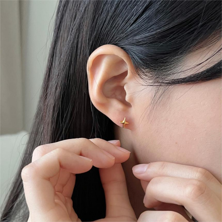 A pair of sparkle stud earrings made with 18k gold plating, featuring a minimalist four-pointed star design, displayed on a dark velvet fabric with small gold dots. These celestial earrings are available in Ottawa, Ontario, Canada.