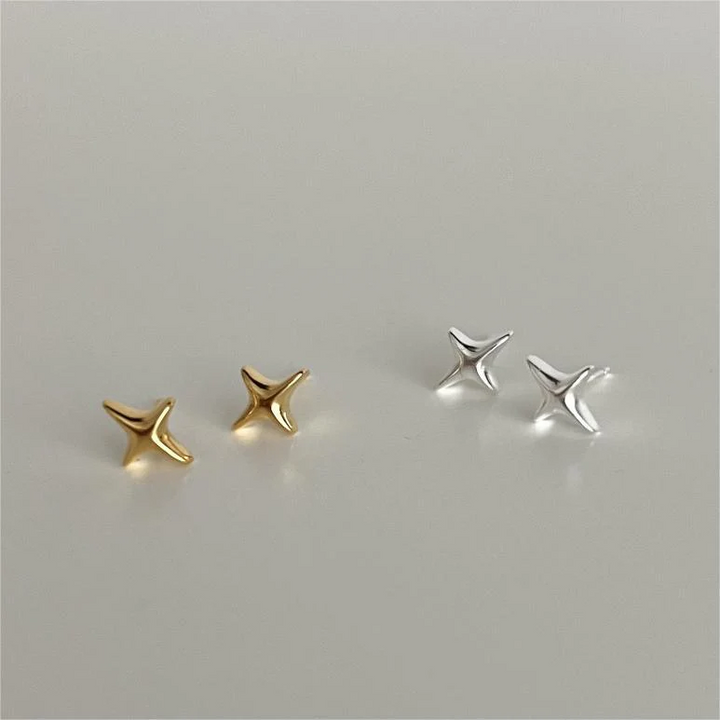 A set of silver and gold sparkle stud earrings, each featuring a minimalist four-pointed star or starfish-like design, displayed on a light grey surface. These celestial earrings are available in Ottawa, Ontario, Canada.
