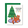 A holiday greeting card with a green envelope behind it. The card features an illustration of a green Christmas tree with colorful lights and a smiling orange tabby cat sitting on a purple blanket, next to the text 'SPREADING HOLIDAY cheer'.