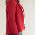 A close-up side view of a person wearing a red cropped sweatshirt or jacket with a white side panel, paired with blue jeans against a light neutral background.