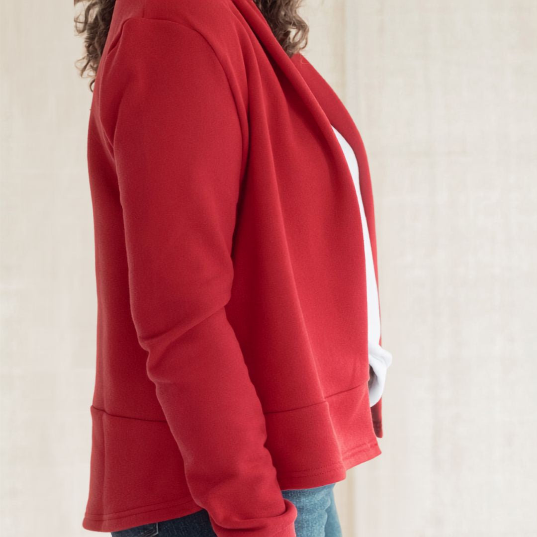 A close-up side view of a person wearing a red cropped sweatshirt or jacket with a white side panel, paired with blue jeans against a light neutral background.