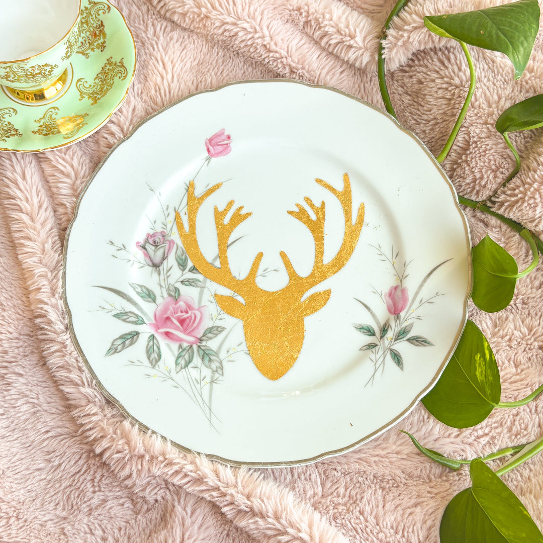 Decorative plate with gold deer head design on a textured surface with leaves.