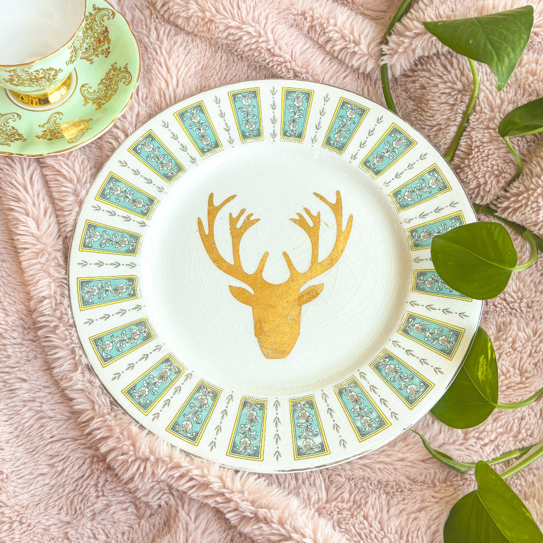 Decorative plate with gold deer design on a textured surface with leaves.