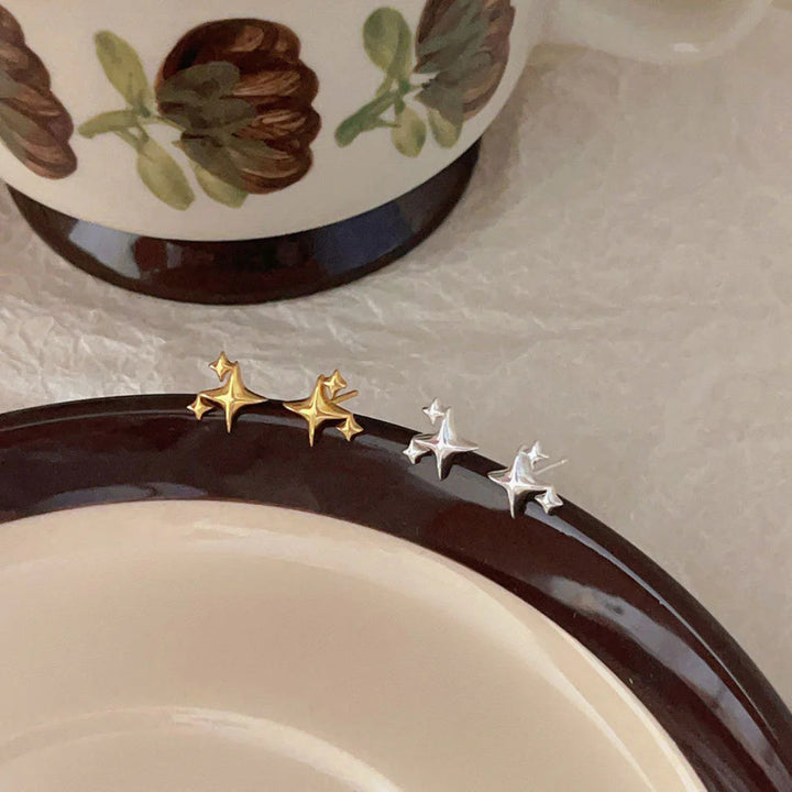 A set of gold and silver-plated star stud earrings, featuring a minimalist star design, displayed on the rim of a ceramic plate. These are celestial and elegant earrings, available in Ottawa, Ontario, Canada.
