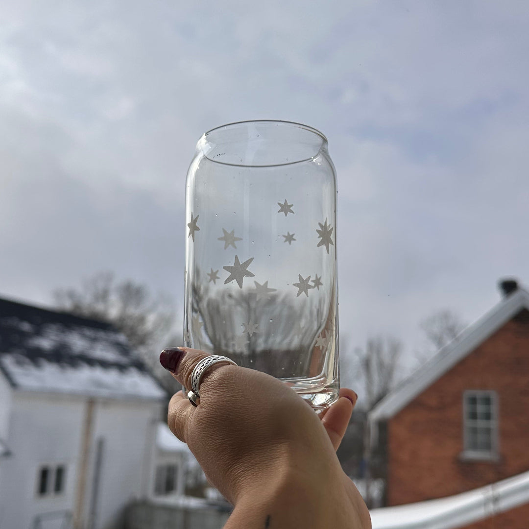 Hand holding a clear glass with star designs outdoors on a snowy day.