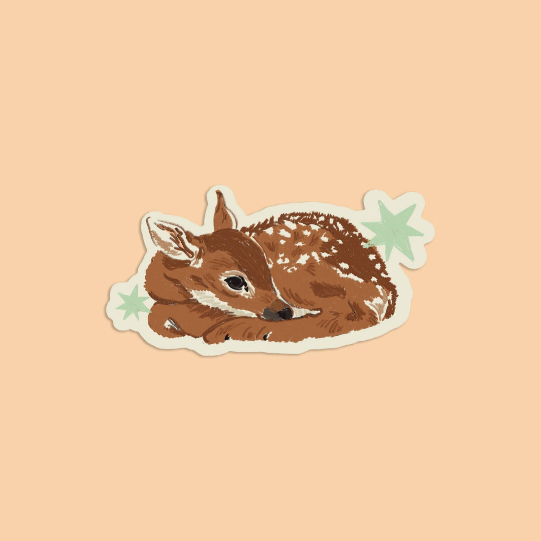 A die-cut sticker featuring an illustration of a sleeping brown fawn with white spots, accented by two light green stars, shown on a solid peach background.