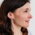 Woman with long brown hair wearing earrings and a necklace against a plain background