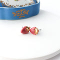 Pink strawberry-shaped earrings on a white plate with a floral-patterned dish in the background.