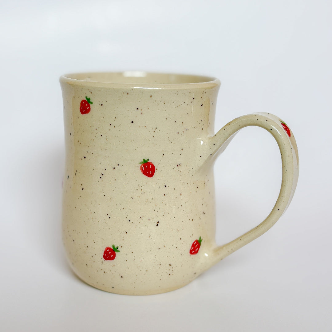 A handmade ceramic mug by Valerie Daoust Ceramics, featuring hand-painted red strawberries on a speckled cream background, displayed on a light gray background. The mug has a large, rounded handle, a speckled texture, and is made in Mississippi Mills, Ontario, Canada.