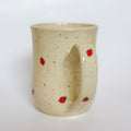 A handmade ceramic mug by Valerie Daoust Ceramics, featuring hand-painted red strawberries on a speckled cream background, displayed on a light gray background. The mug has a large, rounded handle, a speckled texture, and is made in Mississippi Mills, Ontario, Canada.