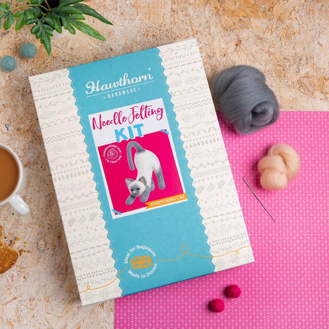 Needle felting kit on a pink mat with a cup of coffee and yarn balls on a textured surface