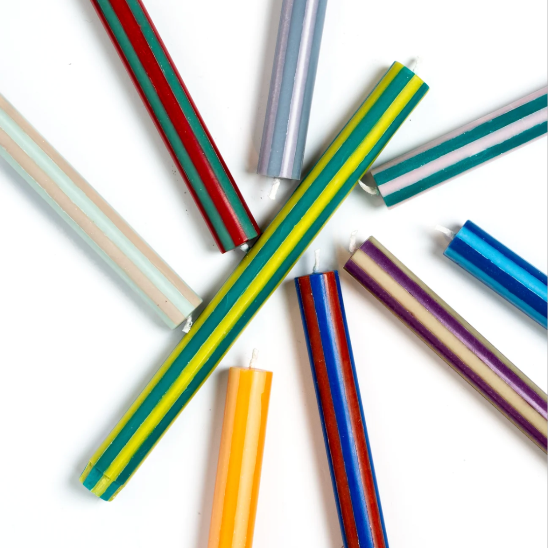 A group of colorful striped taper candles arranged in a starburst pattern on a plain white background.