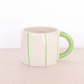White mug with green stripes and handle on a beige surface