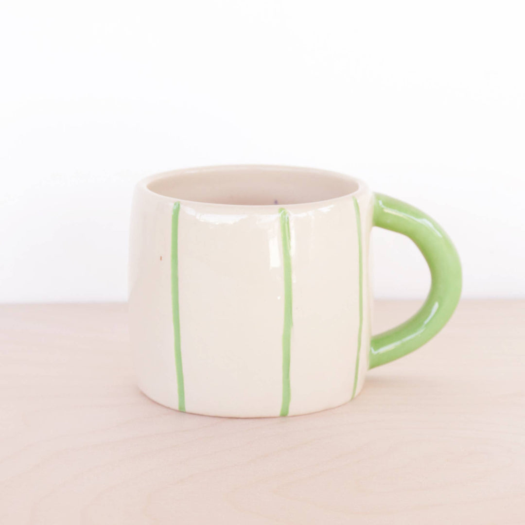 White mug with green stripes and handle on a beige surface