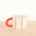 White mug with red handle and red stripes on a beige surface