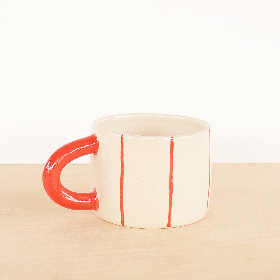White mug with red handle and red stripes on a beige surface