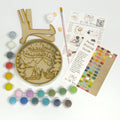 Wooden ornament with engraved design, paint tubes, brushes, and instructions on a white background